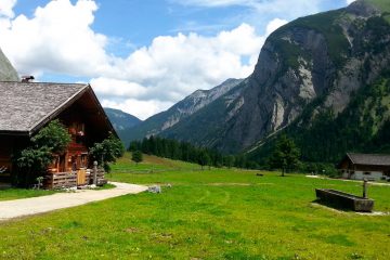 brown wooden house on green grass field near mountain under blue sky